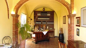 A bar area with a brick archway, a wooden counter, and a wine rack filled with bottles. - Agriturismo Poggio al Sole, Vinci (Vinci)