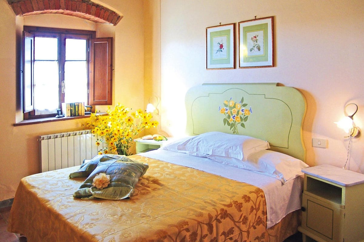 A neatly made bed with a floral bedspread, a bedside table with a lamp, and a window with curtains.
