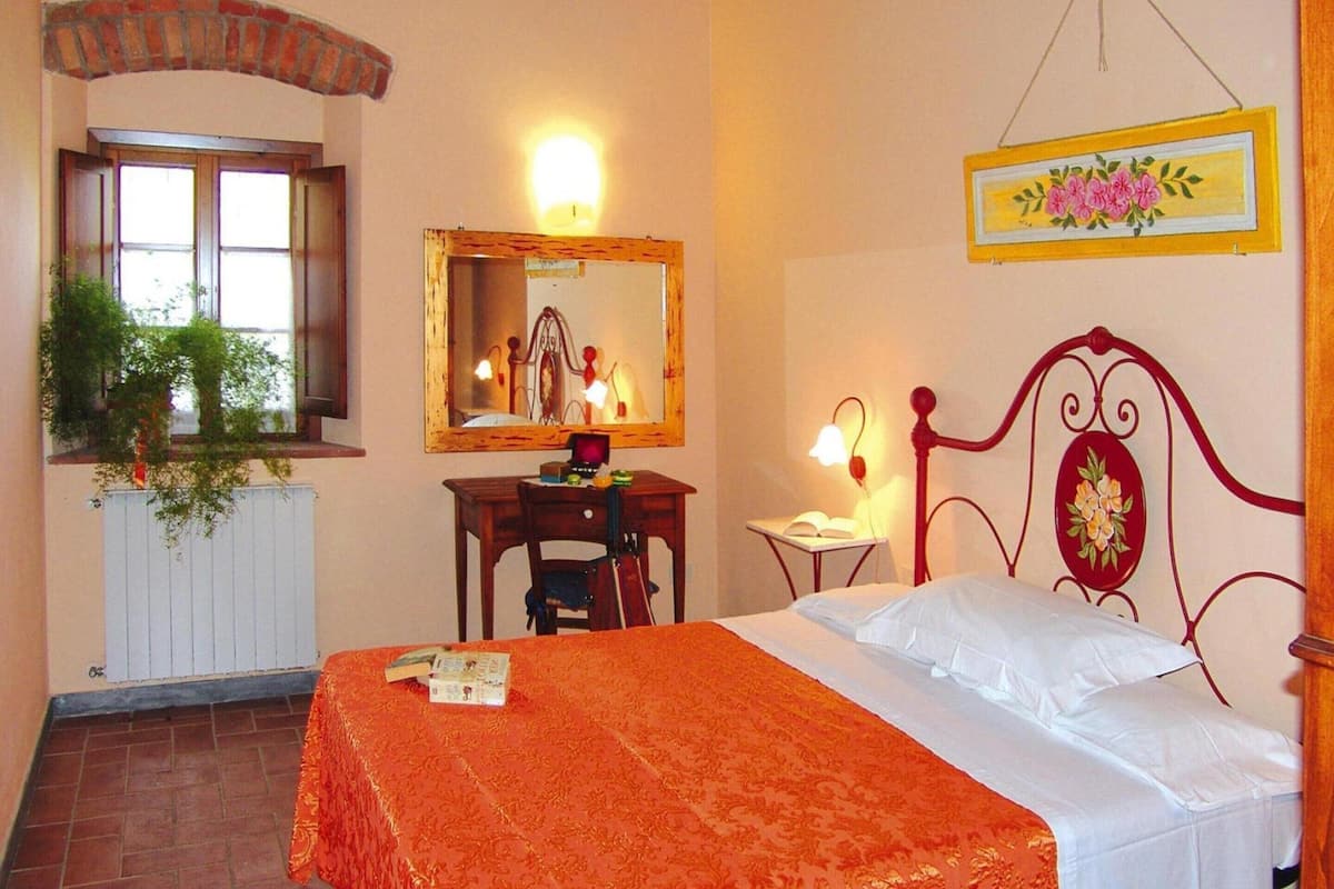 Un dormitorio con cama, escritorio, silla, espejo y ventana con vista a zonas verdes.