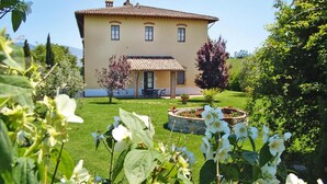 A two-story house with a tiled roof, a small porch, and a garden with flowering plants. - Agriturismo Poggio al Sole, Vinci (Vinci)