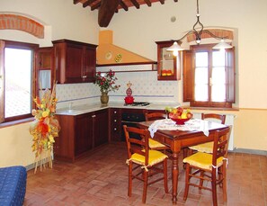 Una cocina con armarios de madera, una mesa de comedor con sillas, un jarrón de flores y una lámpara colgante.
