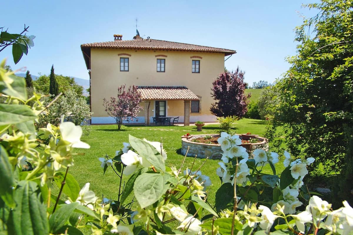 A two-story house with a tiled roof, a front porch, and a well-maintained garden with flowering plants and a circular flower bed.