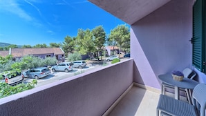 A balcony with a view of parked cars and trees, a table with chairs, and a small plant on the table. - Apartments Medena in Seget Donji, Trogir (Seget)