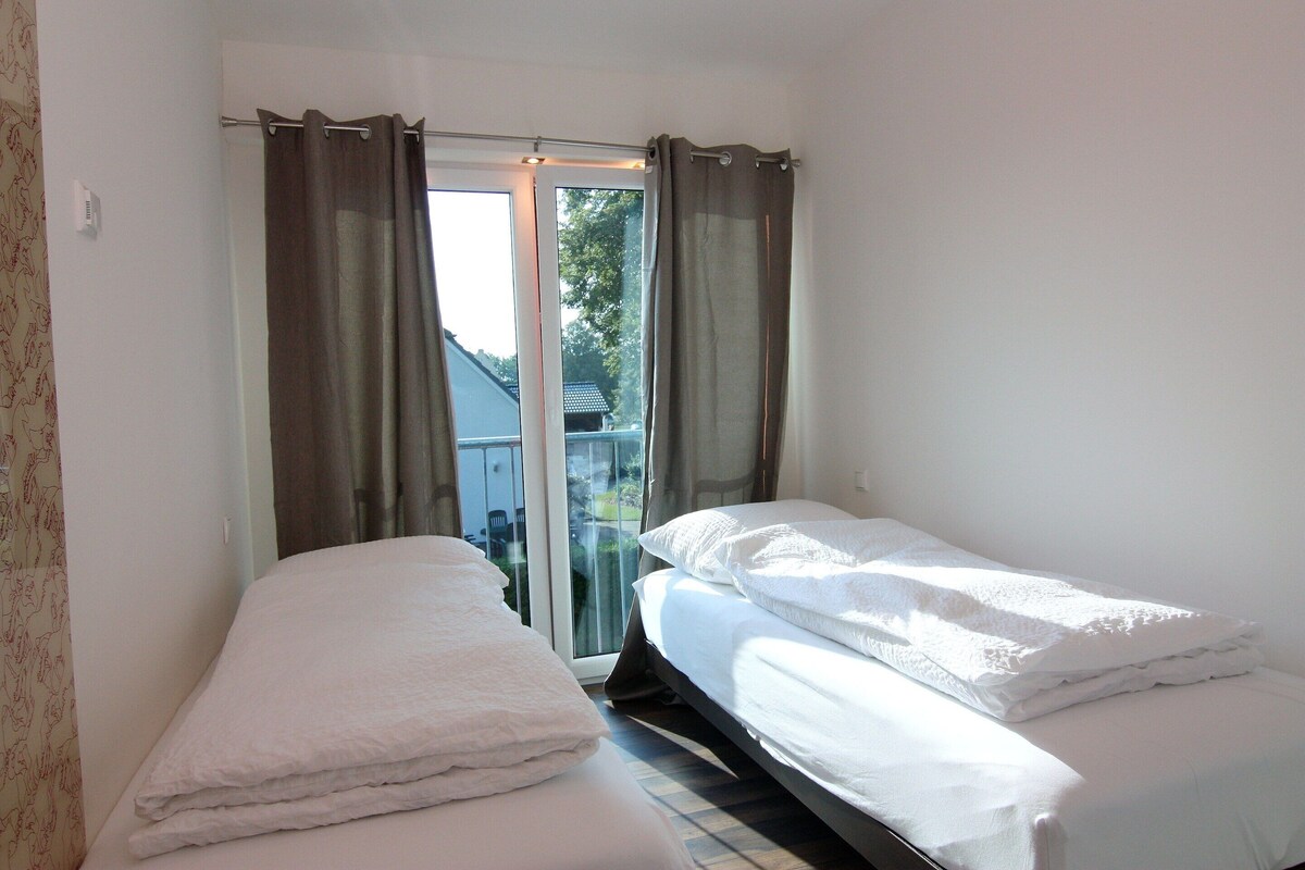 Ein kleines, sauberes Zimmer mit zwei Einzelbetten, einem fensterbelaubten Fenster und Blick nach außen.