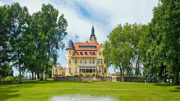Ein großes, gelbes Gebäude mit einem Turm und einem Brunnen im Vordergrund.