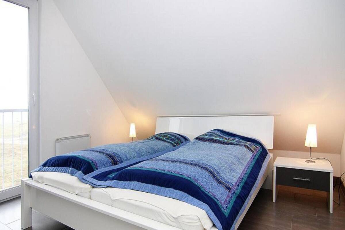 Una camera da letto moderna con un letto bianco, due comodini con lampade e un'ampia finestra.