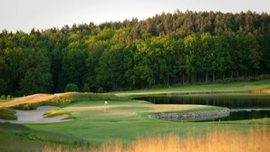 A golf course with a flag, sand bunkers, a pond, and a forested backdrop. - Holiday Home Oliver, Wendorf (Kuhlen-Wendorf)