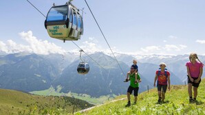 Un téléphérique portant l'inscription « Wild Kogel Bahnen » dans une région montagneuse, avec des randonneurs à proximité.