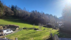 A rural landscape with a grassy field, a wooden fence, a white van, and a small building with a sloped roof. - Apartment in Neukirchen With a Balcony (Neukirchen am Grossvenediger)