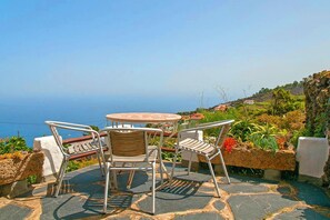 A patio with a table and chairs, a view of the sea, and a stone pathway. - Finca La Hoya, El Tanque (El Tanque)