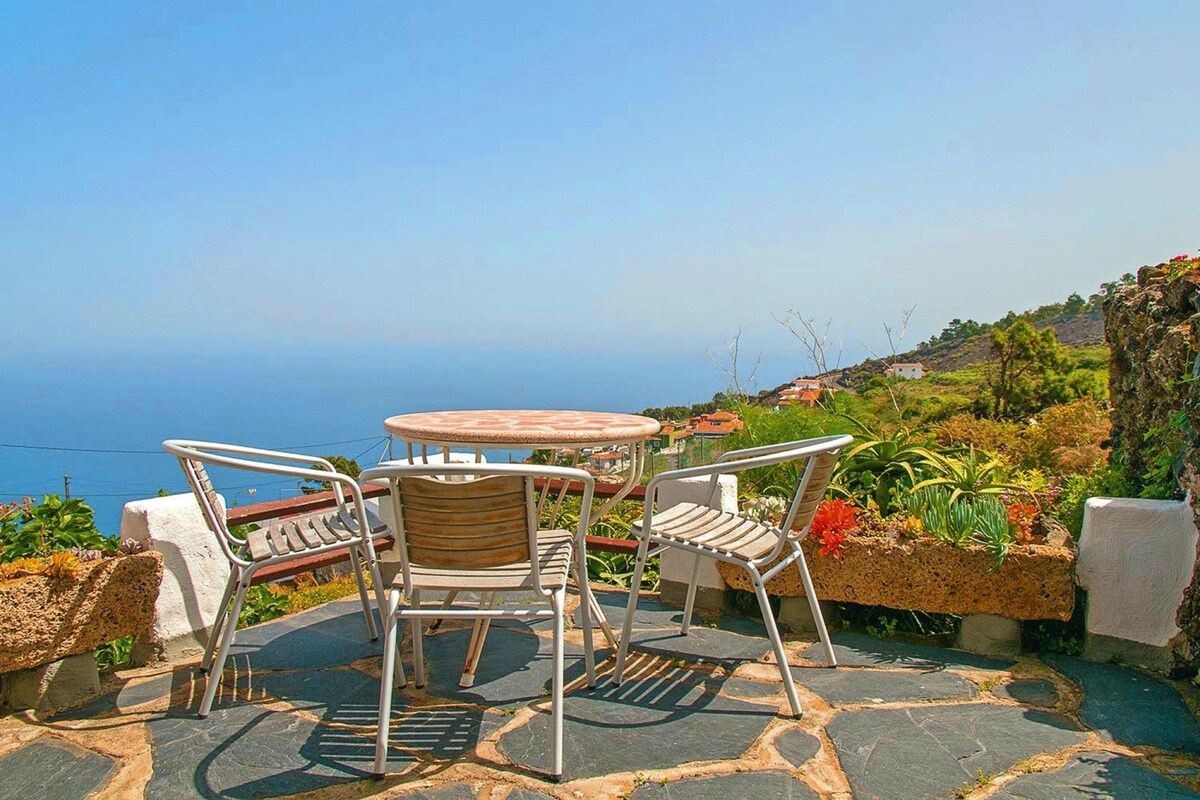 A patio with a table and chairs, a view of the sea, and a stone pathway.