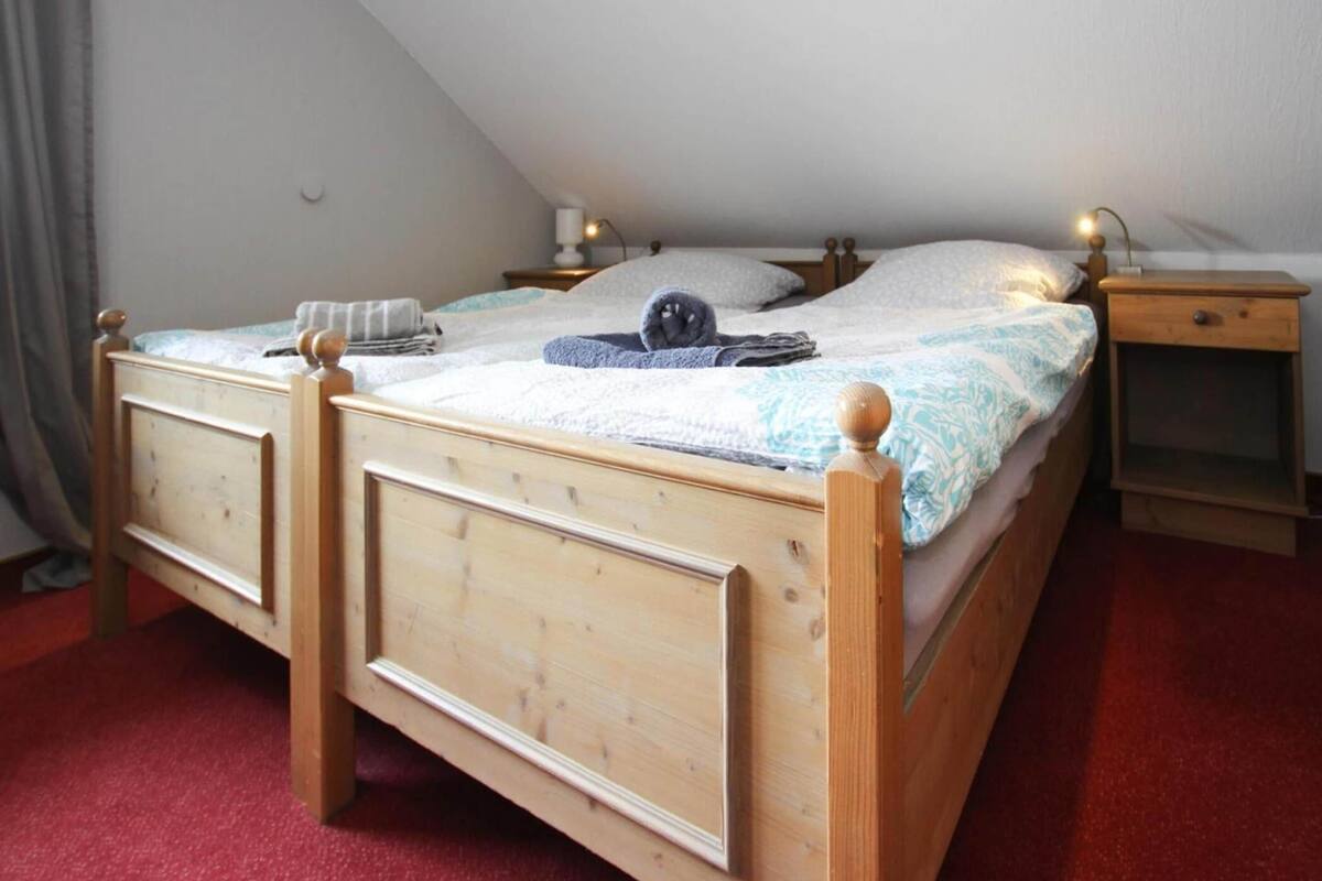 A wooden bed with a headboard, a bedside table, and a nightstand in a room with a sloped ceiling.