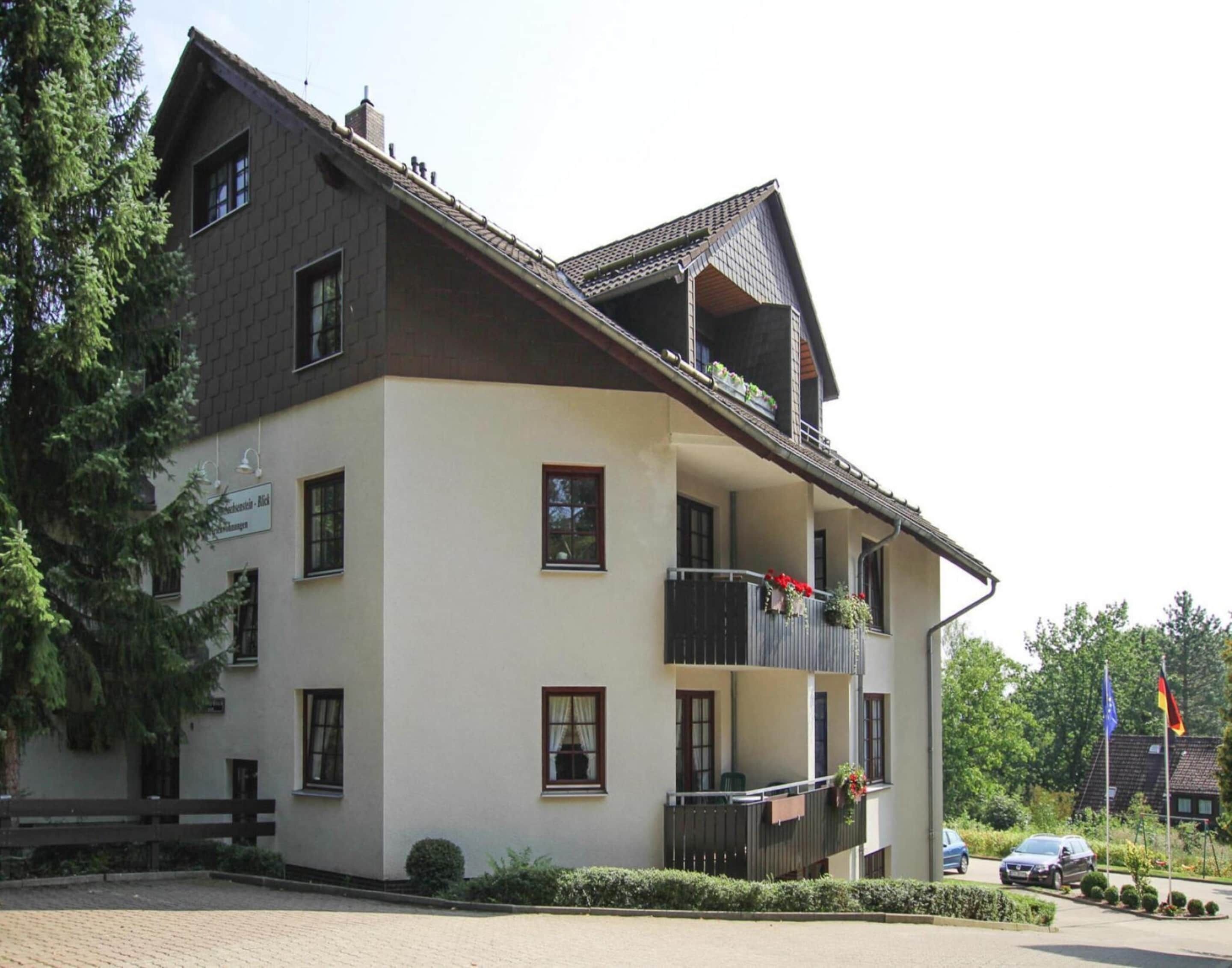 Ein mehrstöckiges Gebäude mit einem Balkon im zweiten Stock, einem Schild, das ein Restaurant anzeigt, und einem Parkplatz mit Autos.