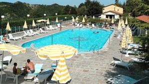 Una piscina con lettini e ombrelloni, circondata da un solarium in pietra e alberi.
