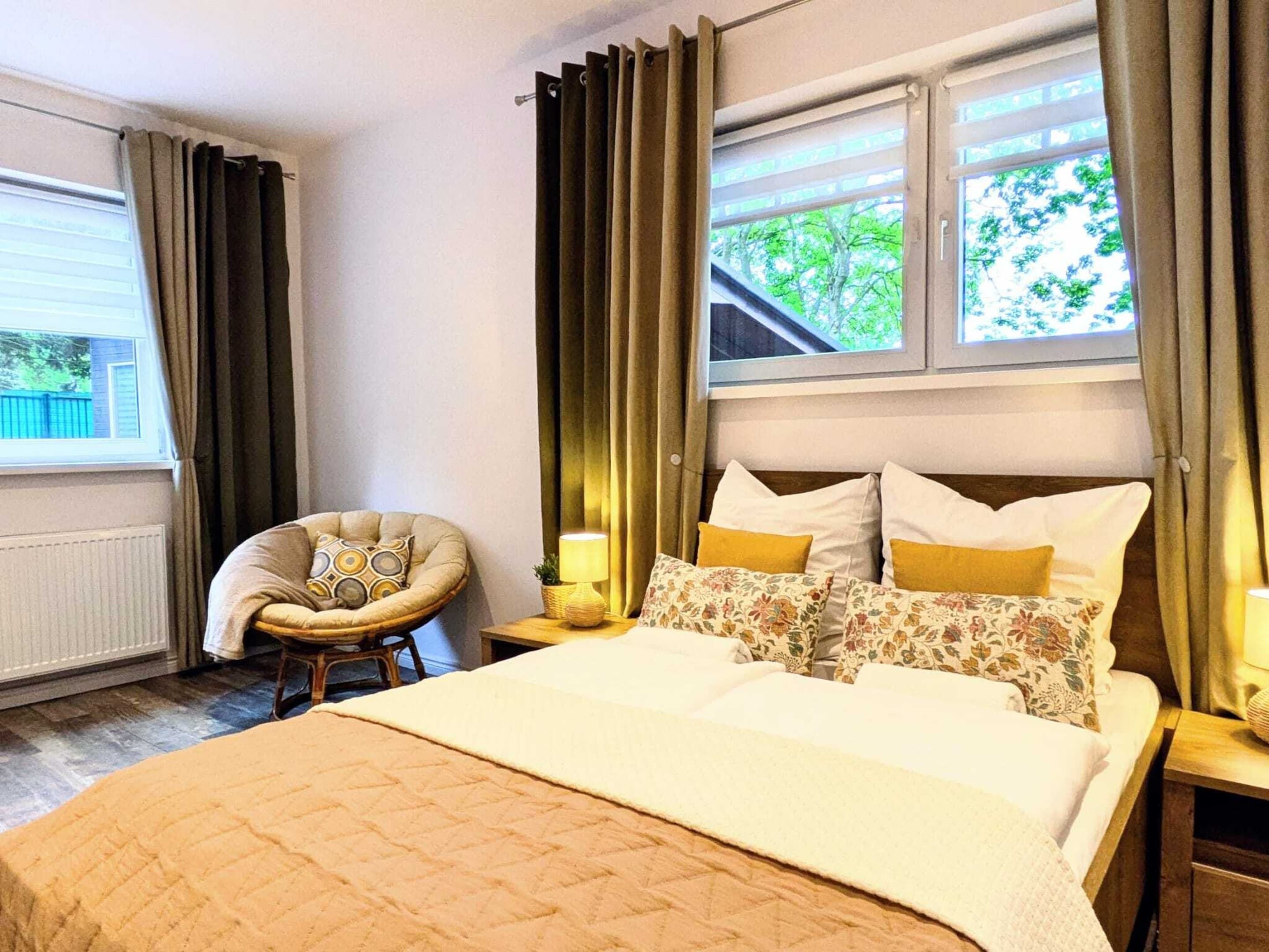 A bedroom with a bed, two bedside tables, a chair, and a window with curtains.