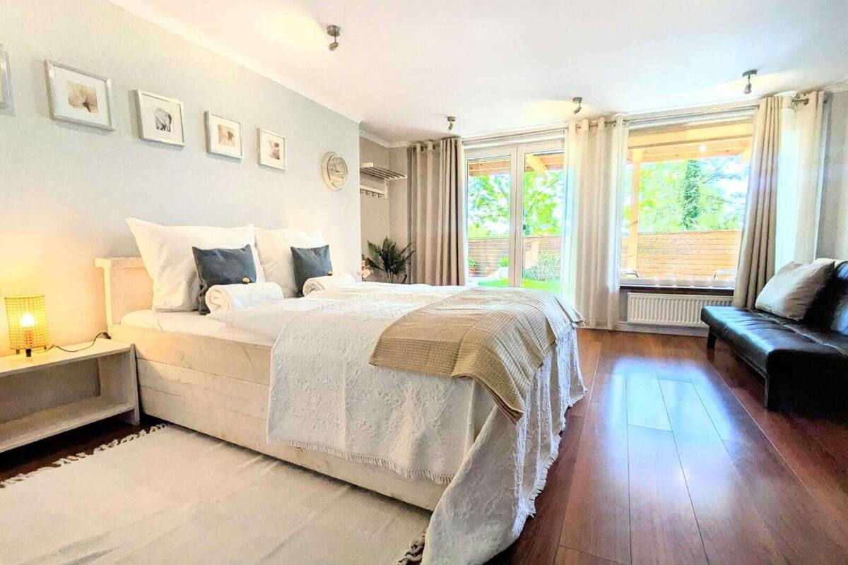 A bedroom with a large bed, a nightstand, a dresser, and a window with curtains.