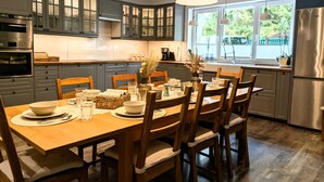 A modern kitchen with grey cabinets, a wooden dining table, and a large window providing a view of the outdoors.