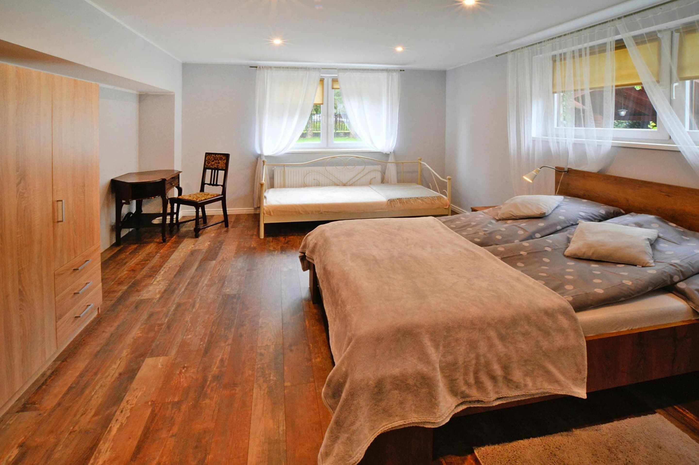 Een slaapkamer met een houten vloer, een bed met dekbedovertrek, een stoel, een tafeltje en een kledingkast.