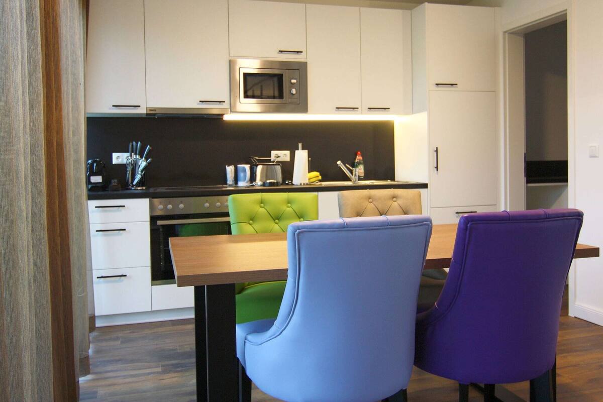 Una cocina moderna con armarios blancos, un microondas y una zona de comedor con una mesa de madera y dos sillas.