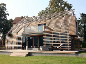 Una casa moderna con fachada de madera en listones, ventanas amplias y techo plano.