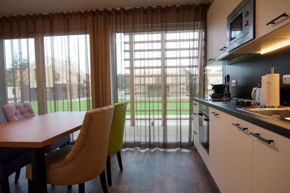 A compact kitchen with a dining area, large windows, and a view of a green outdoor space.