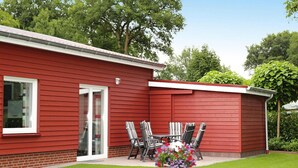 A red building with a glass door and a patio area with chairs and a flower pot. - Ferienwohnung Landblick, Rastede (Rastede)