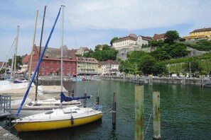 A harbor with boats docked, a red building, and a hill with buildings in the background. - Apartments Am Untertor, Meersburg (Meersburg)