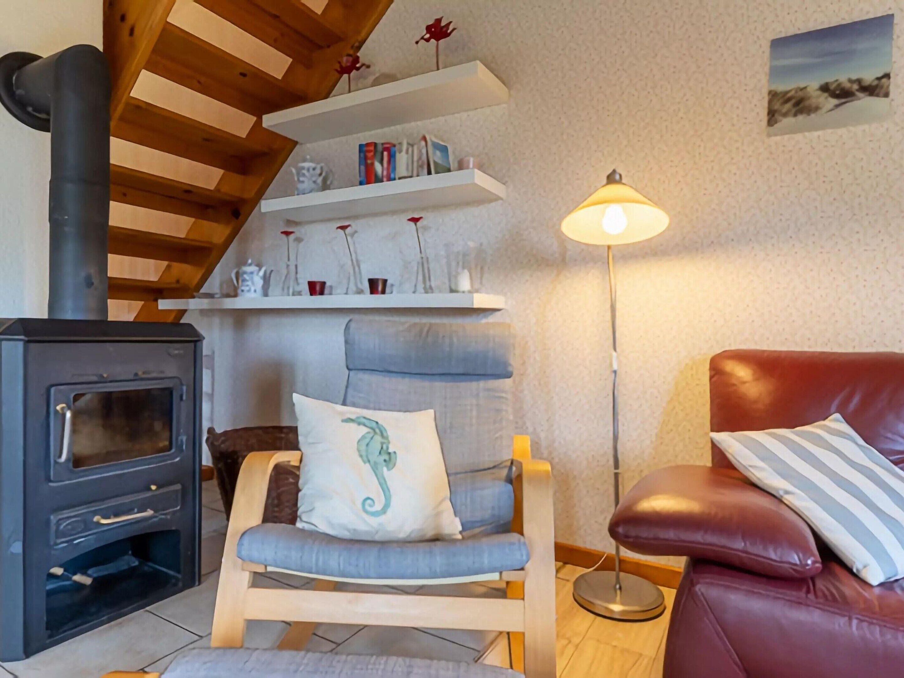 Ein gemütliches Wohnzimmer mit Kaminofen, einem bequemen Sessel mit Kissen, einer roten Ledersofa und einer Stehlampe.