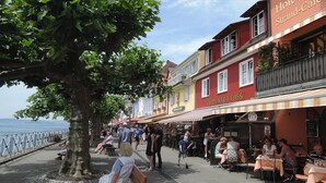 Une promenade en bord de mer avec des terrasses, un sentier bordé d’arbres et un hôtel appelé « Hôtel Strand-Café ».