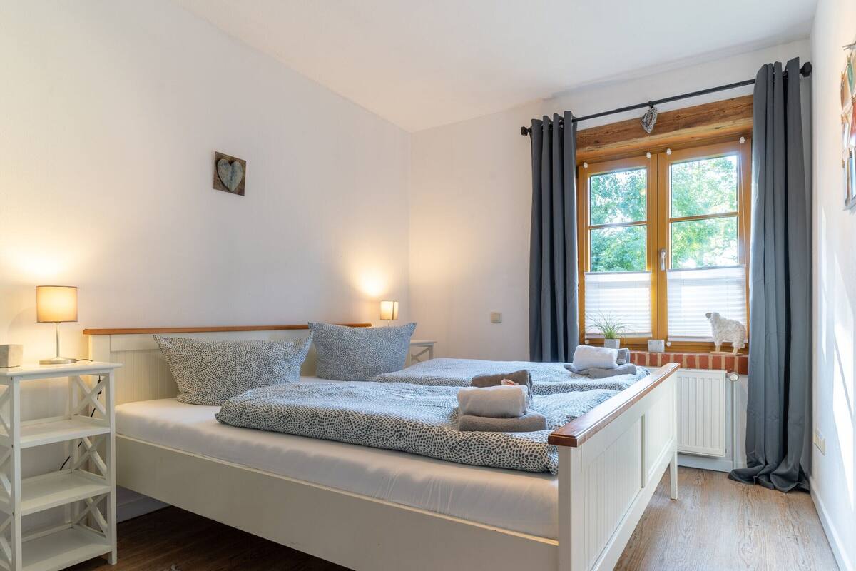 Une chambre à coucher avec un lit, des tables de chevet, une fenêtre avec des rideaux et un radiateur.