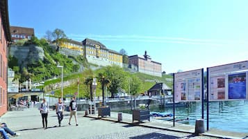 A riverside walkway with benches, a bridge, and buildings in the background.