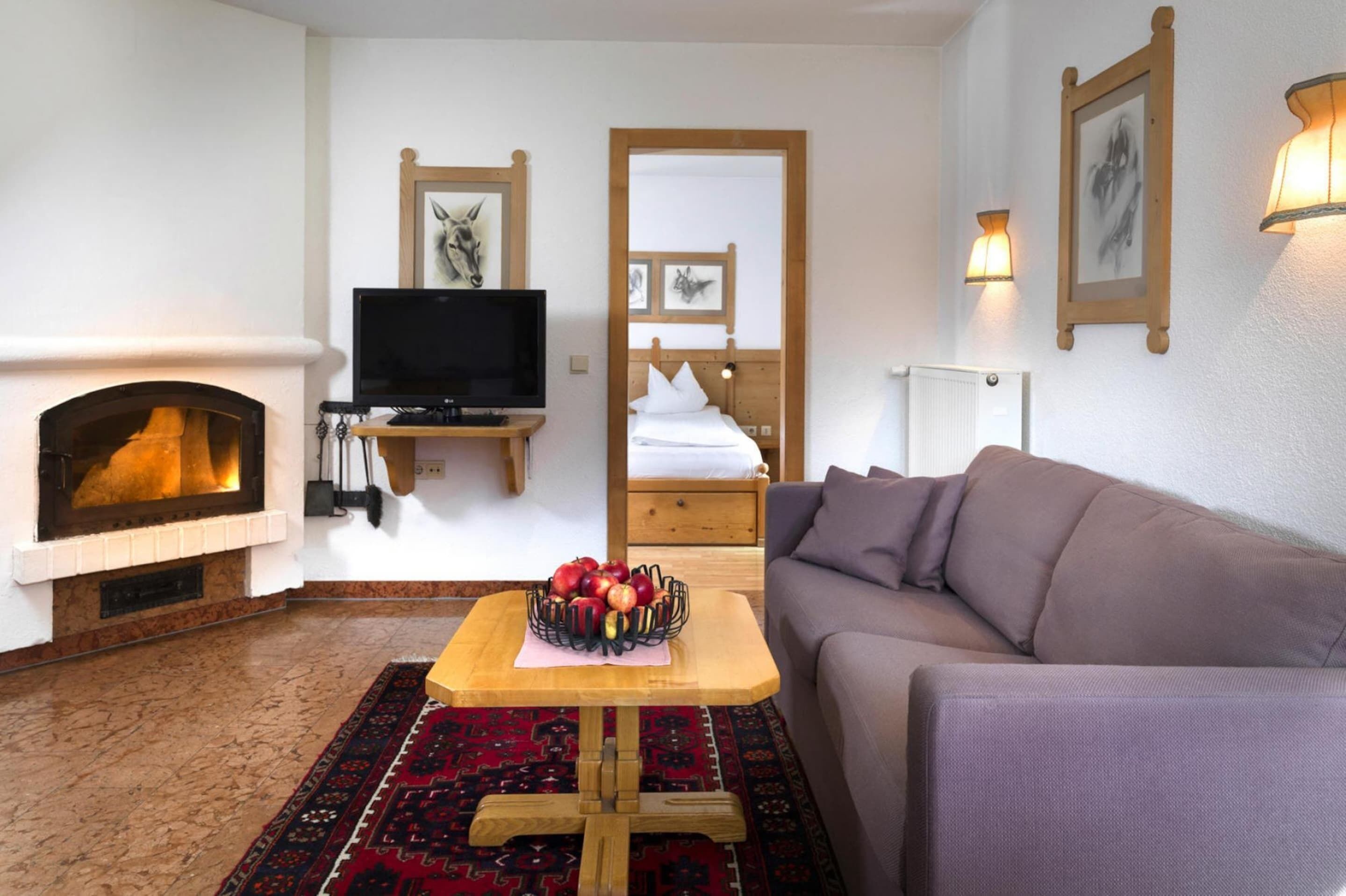 A cozy living room with a fireplace, a television, a sofa, and a table with fruit.