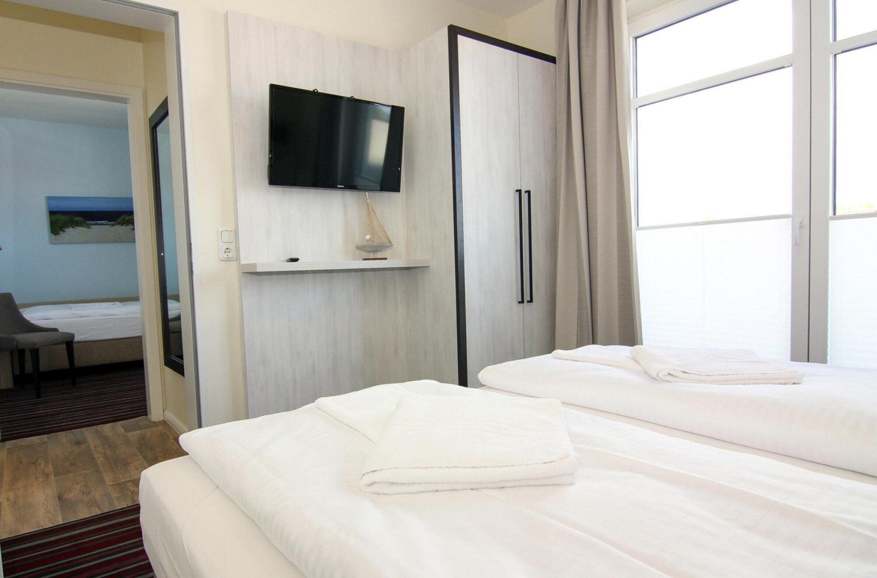 A hotel room with two beds, a flat-screen TV, a desk with a lamp, and a painting on the wall.