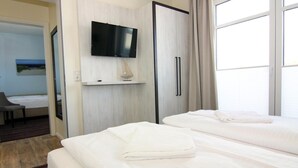 Una camera d'albergo con due letti, una TV a schermo piatto, una scrivania con lampada e un quadro appeso al muro.