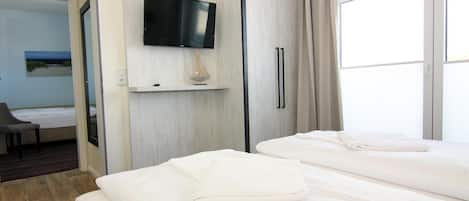 A hotel room with two beds, a flat-screen TV, a desk with a lamp, and a painting on the wall.