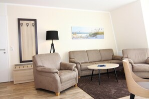 A living room with a beige sofa, a round coffee table, and a lamp. - Apartments in the Avalon Hotel Bellevue, Fehmarn (Fehmarn)