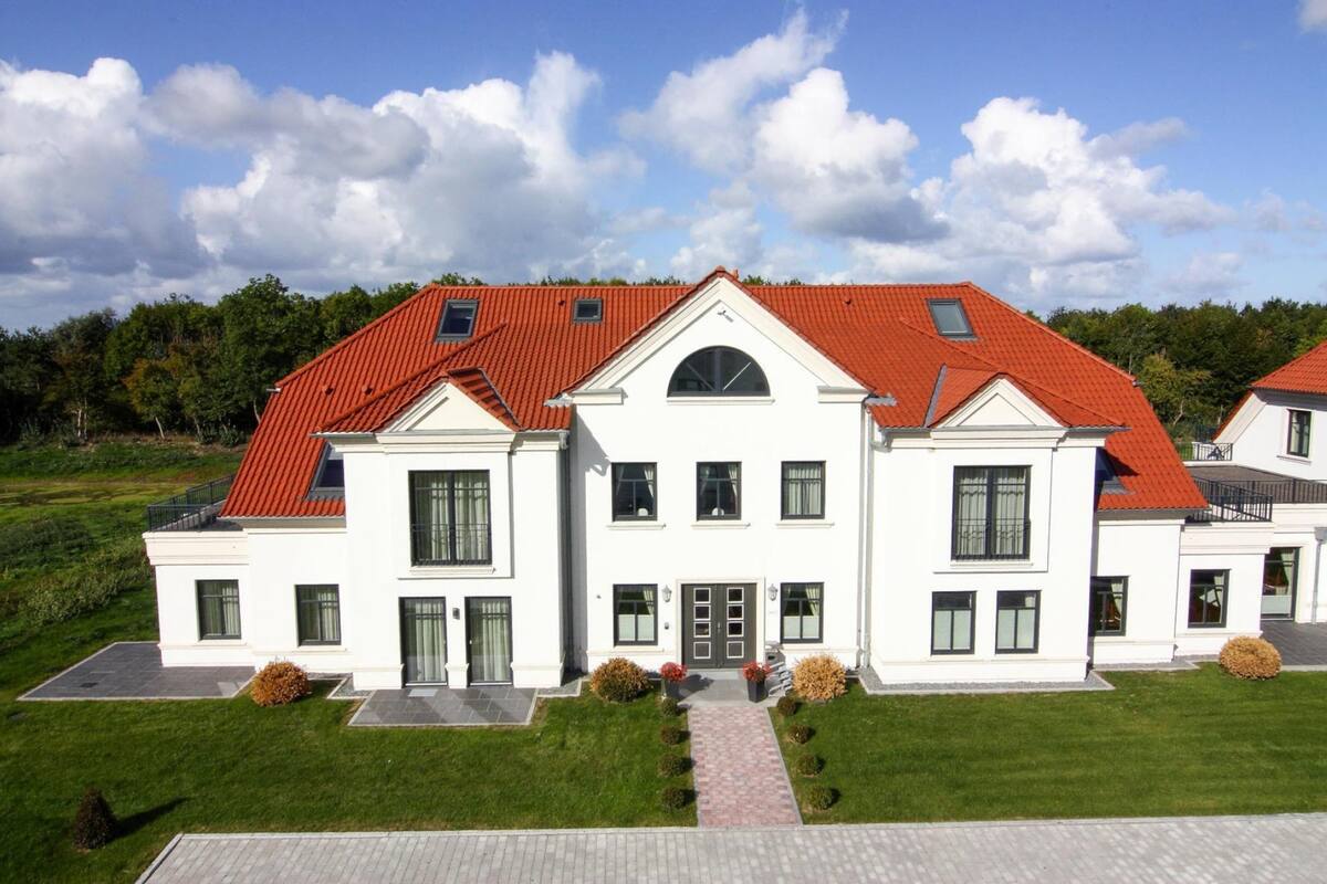 A large, white, two-story house with a red roof, multiple windows, and a paved driveway.
