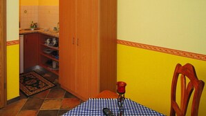 A kitchen with wooden cabinets, a tiled backsplash, and a small dining area with a checkered tablecloth and a chair. - Bungalow in Lubben With a Terrace (Lübben (Spreewald))