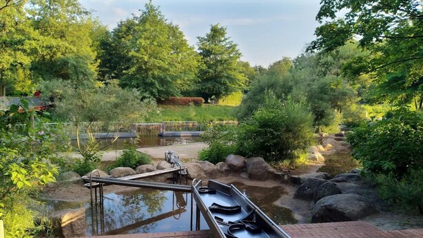 A tranquil outdoor pool area with a small pond, surrounded by lush greenery and a wooden deck. - Bungalow in Lubben With a Terrace (Lübben (Spreewald))