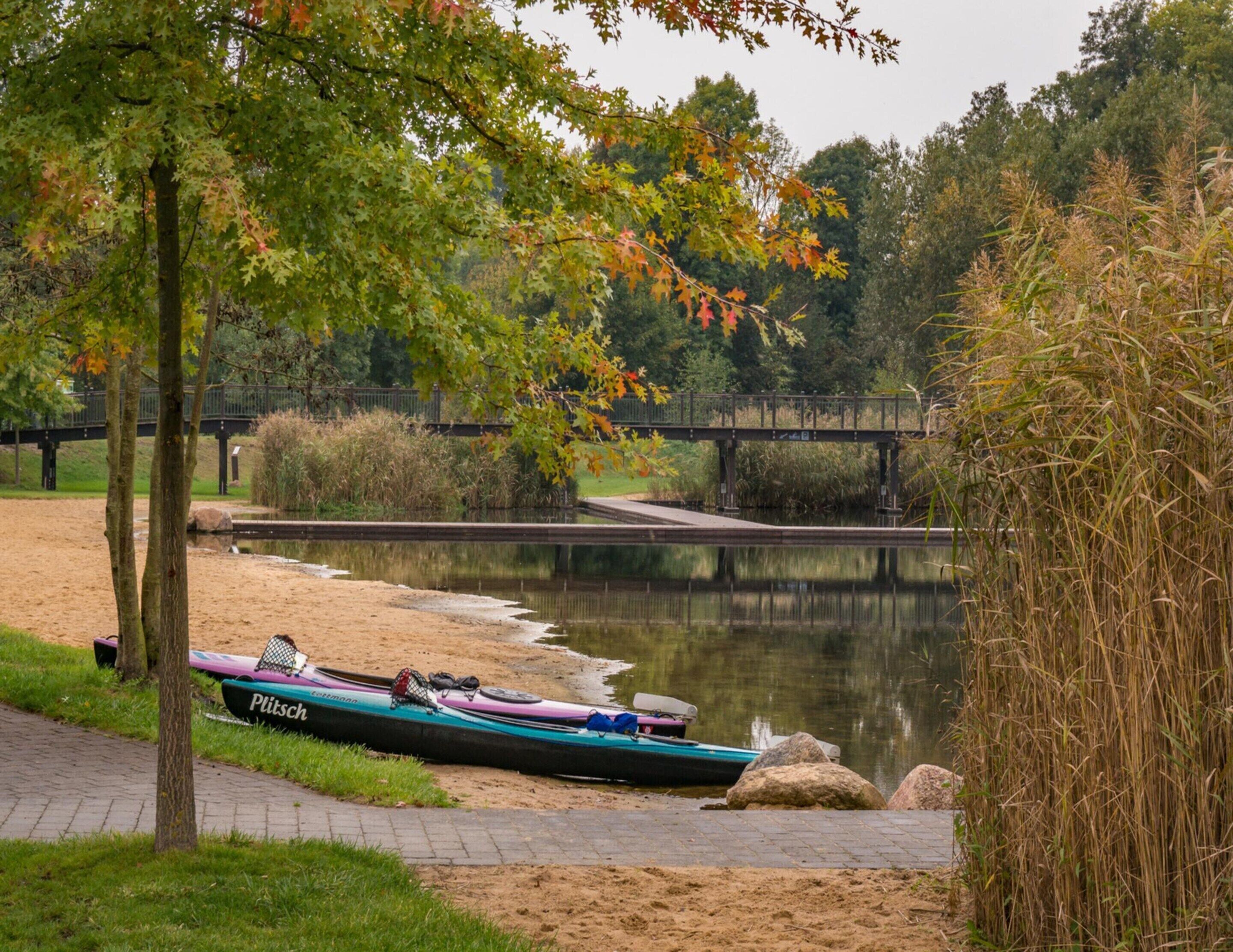 Une rivière paisible, avec un kayak amarré sur la rive, un pont en arrière-plan et un sentier menant à l'eau.