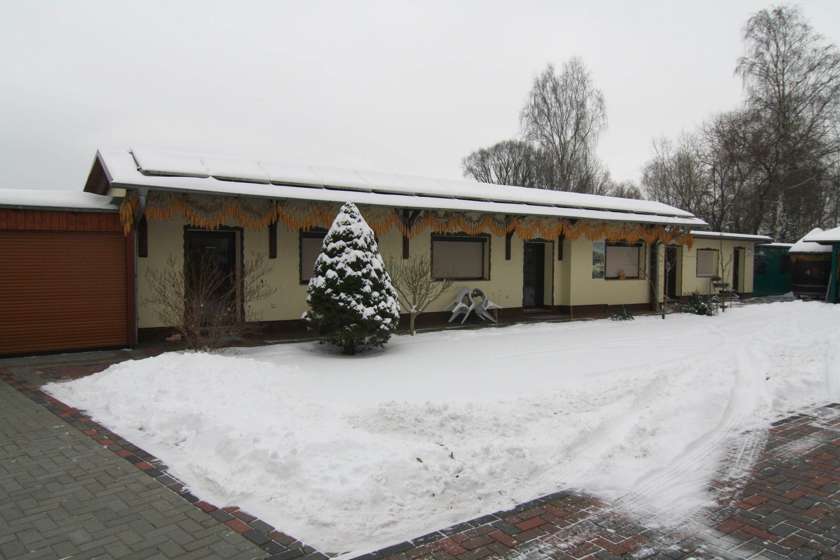Een gebouw met een met sneeuw bedekte dak en een besneeuwde grond. Een boom staat ervoor.