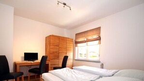 Un dormitorio con cama, escritorio, dos sillas, televisión y armario.