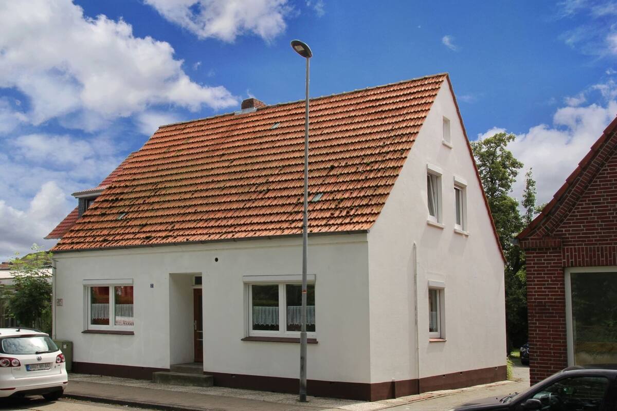 A single-story house with a red-tiled roof, white walls, and a small front porch.