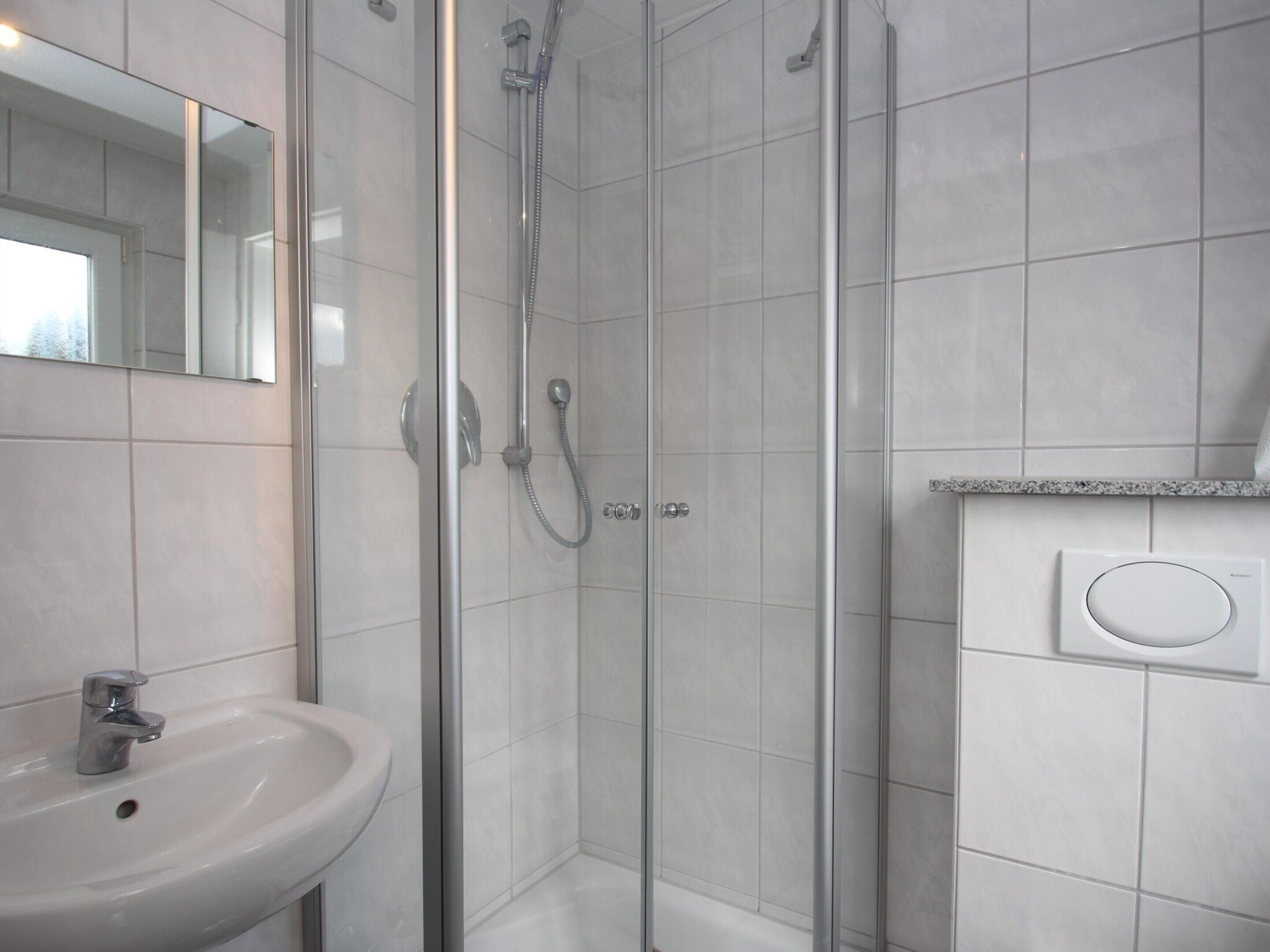 A modern bathroom with a glass-enclosed shower, a white sink, and a mirror.