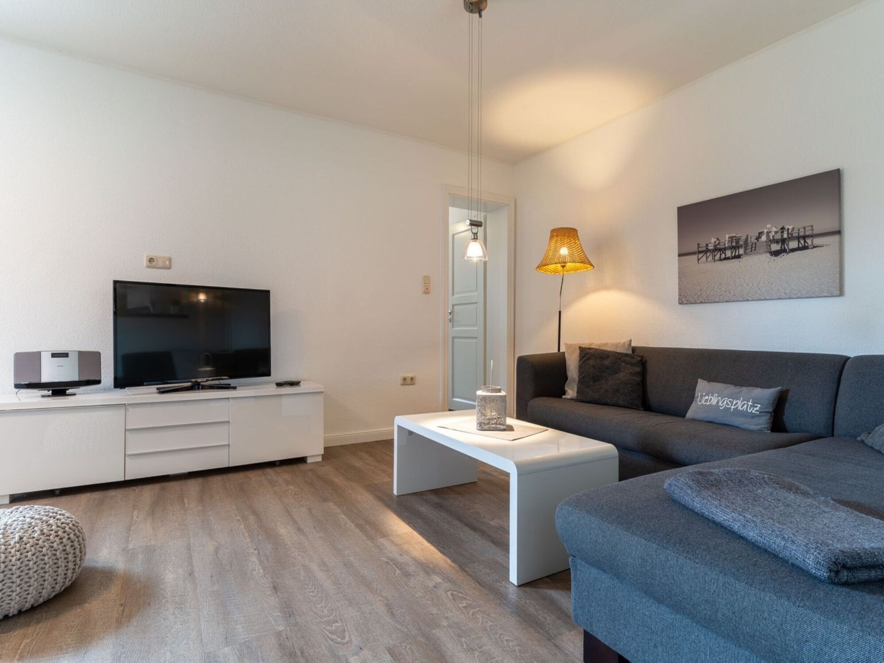 Un salon moderne avec un téléviseur à écran plat, une table basse blanche, un canapé gris et une lampe.