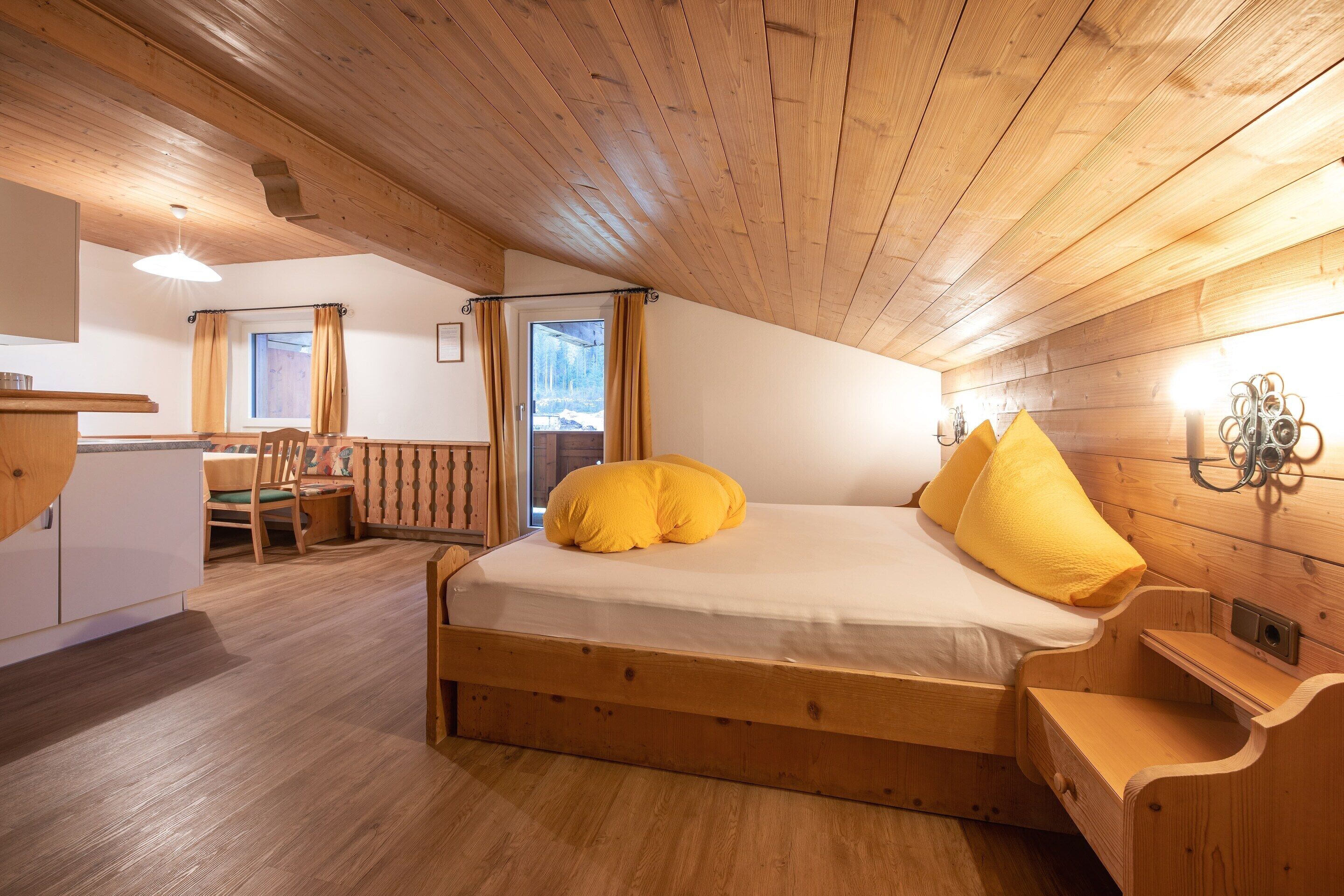 A wooden room with a bed, a dining table, and chairs.