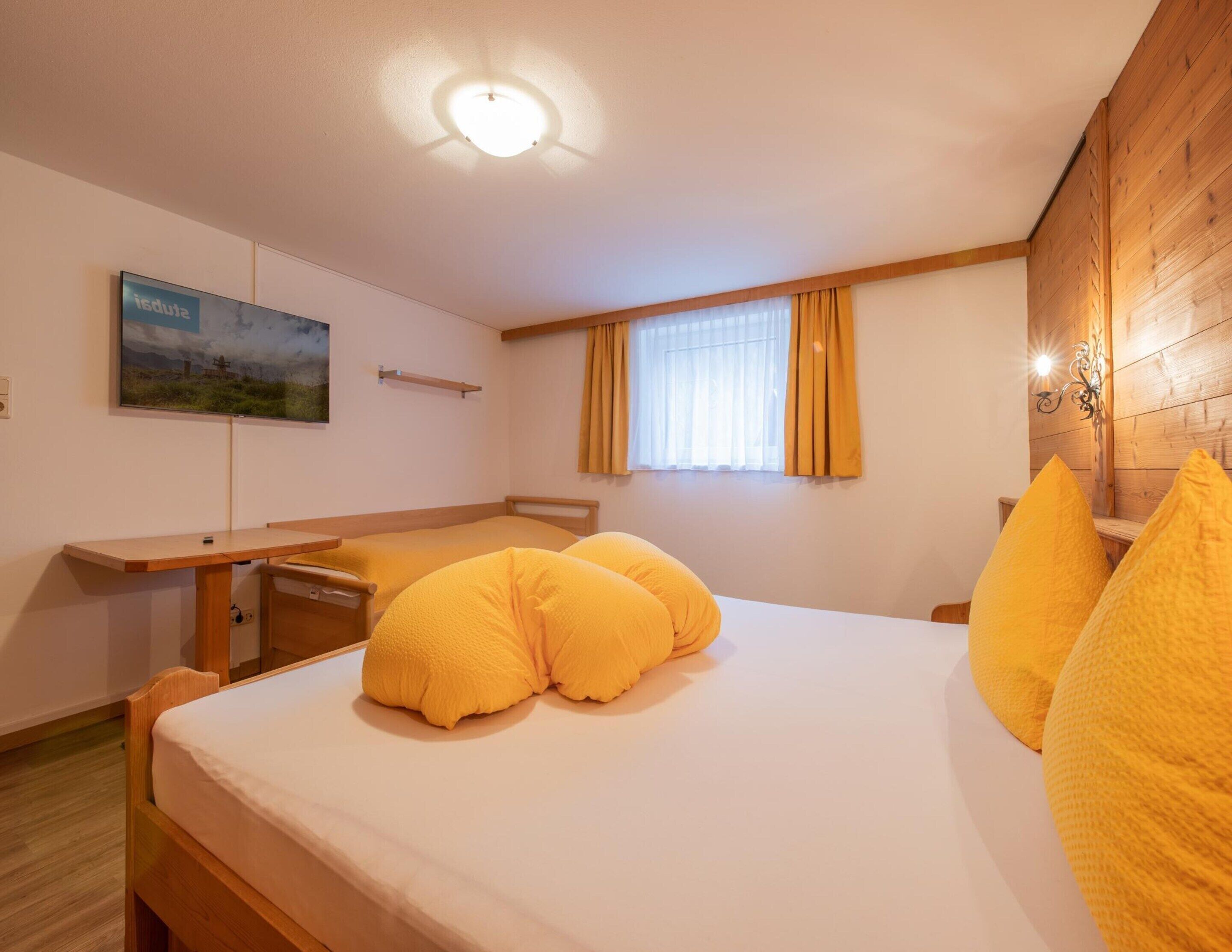 A bedroom with a wooden bed, a desk, a window with curtains, and a painting on the wall.
