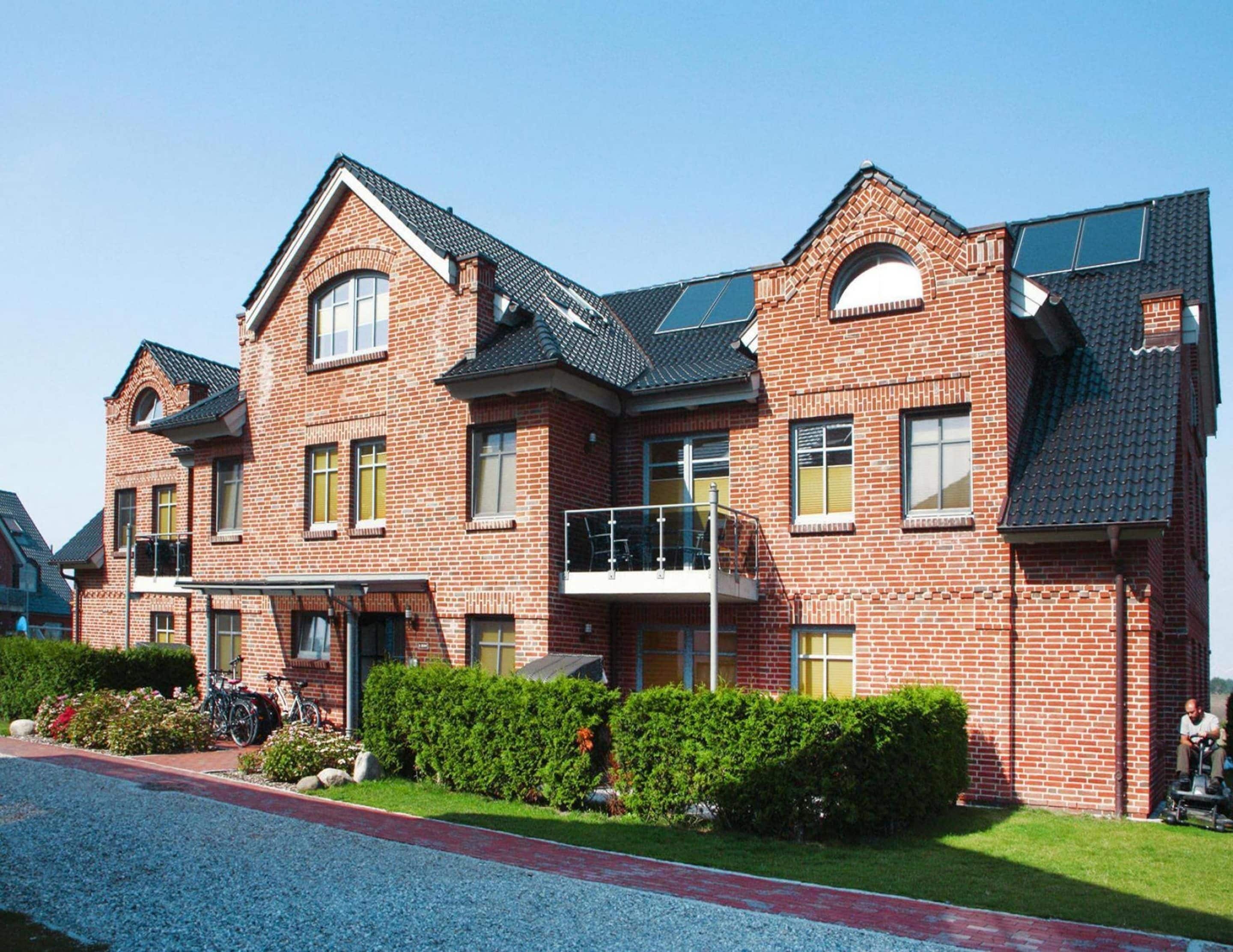 A multi-story brick building with a balcony, a gravel driveway, and a well-maintained lawn.