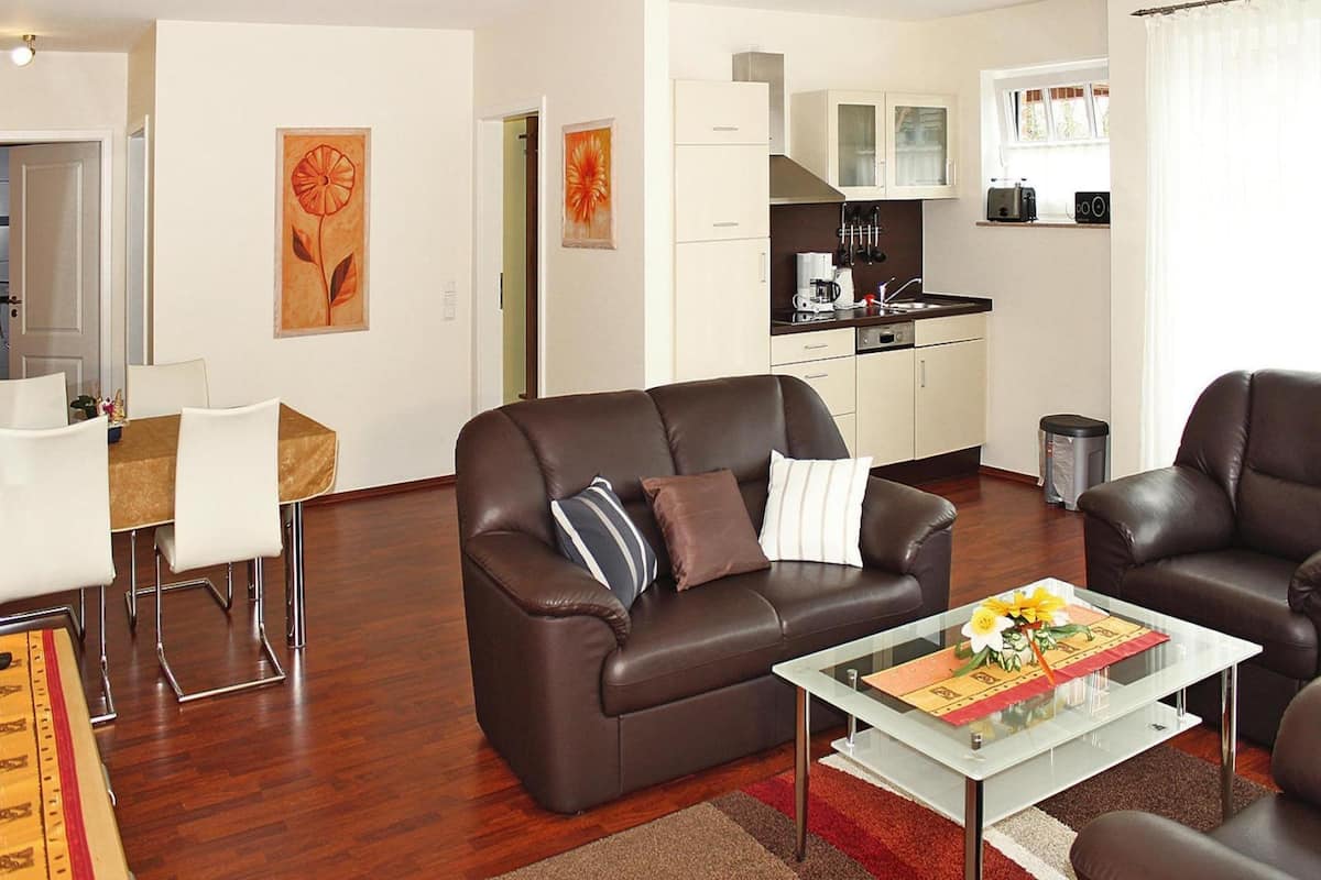 A modern living room with a brown leather sofa, a glass coffee table, and a dining area with a white table and chairs.