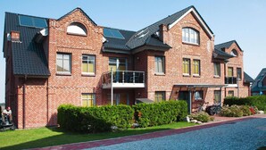 A multi-story brick building with a balcony, a covered porch, and a gravel driveway. - Aparthotel Museumshof, Fehmarn (Fehmarn)